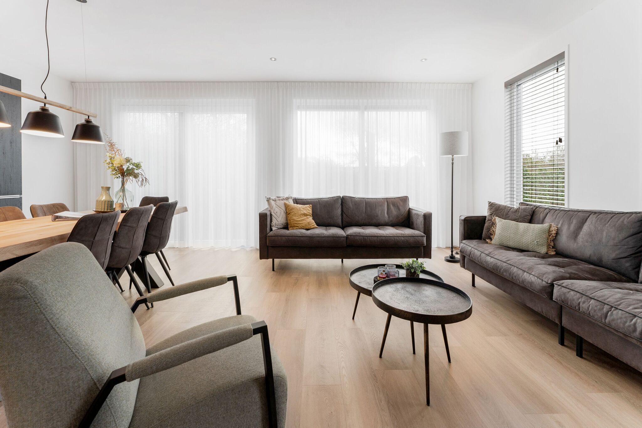 Een moderne woonkamer met een bank, fauteuils, een salontafel en een eethoek met stoelen en een tafel.