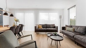 Ein modernes Wohnzimmer mit einer Couch, Sesseln, einem Couchtisch und einem Essbereich mit Stühlen und Tisch.