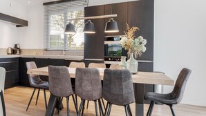 Eine moderne Küche mit einem Holzespeisetisch, vier grau gepolsterten Stühlen und Pendelleuchten.