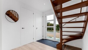 Ein modernes Interieur mit einer Holztreppe, einem runden Spiegel und einer Tür zu einem Außenbereich.