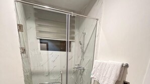 Une salle de bain avec une douche à parois de verre, des toilettes blanches et un porte-serviettes avec une serviette blanche.