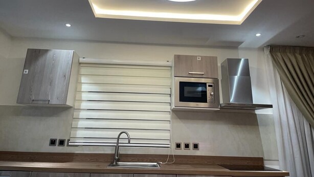 Une cuisine moderne dotée d’un îlot central, d’un four à micro-ondes encastré, d’une hotte en acier inoxydable et d’un luminaire encastré dans le plafond.