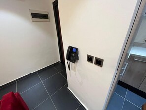 A hotel room with a telephone, a small air conditioning unit, and a door leading to another room. - Park Apartments D-plus One bed+Living room - Cantonments  (Accra)