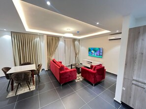 Sala de estar moderna com área de jantar, televisão de tela plana na parede e uma janela grande com cortinas.