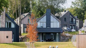 Un immeuble résidentiel moderne doté d’une grande façade vitrée, d’un revêtement extérieur en pierre et d’une petite terrasse avec des chaises longues.