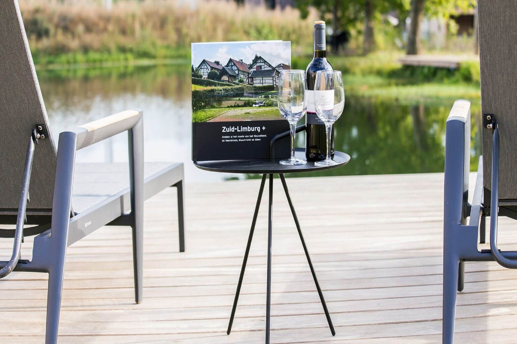 Une table avec une bouteille de vin et deux verres posés sur un présentoir, un panneau indiquant un point de vue panoramique, et une terrasse en bois avec des chaises.