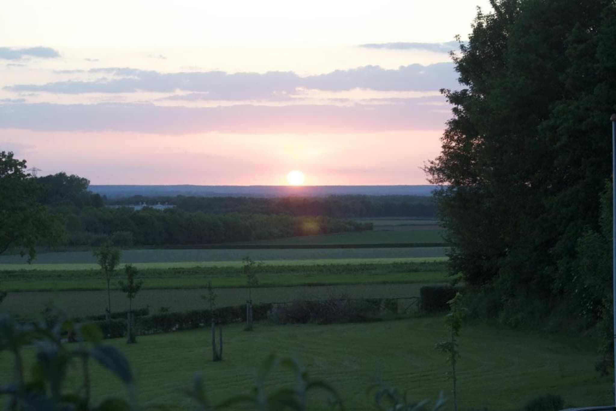 Un coucher de soleil sur un paysage rural, avec des champs et des arbres.