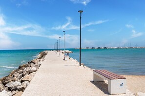 Um calçadão costeiro com bancos e postes de luz, que leva ao mar.