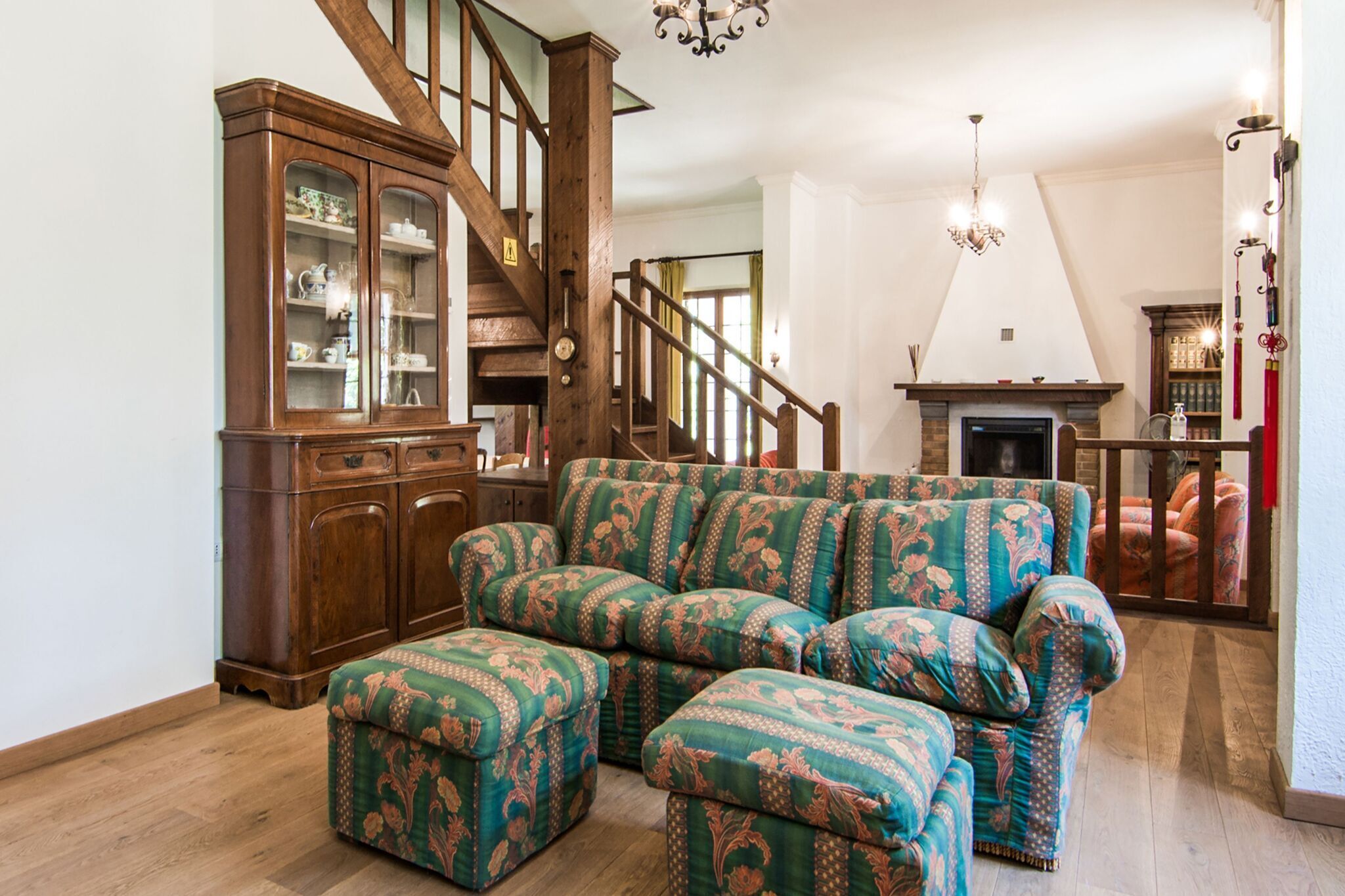 Ein geräumiges Wohnzimmer mit einer Holztreppe, einem Kamin und einem großen, grünen Polstersofa mit passendem Hocker.