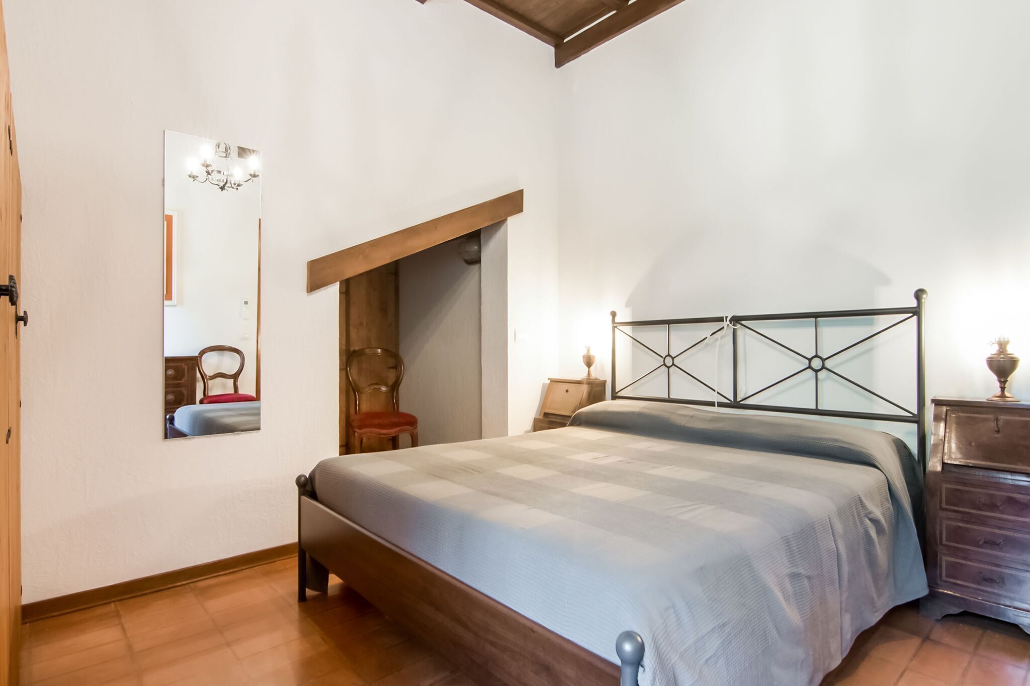 Ein Schlafzimmer mit einem hölzernen Bettgestell, einem Nachttisch, einer Kommode und einem Spiegel an der Wand.