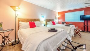 Ein Hotelzimmer mit zwei Betten, einem Flachbildfernseher, einer Stehlampe und einem kleinen Tisch.