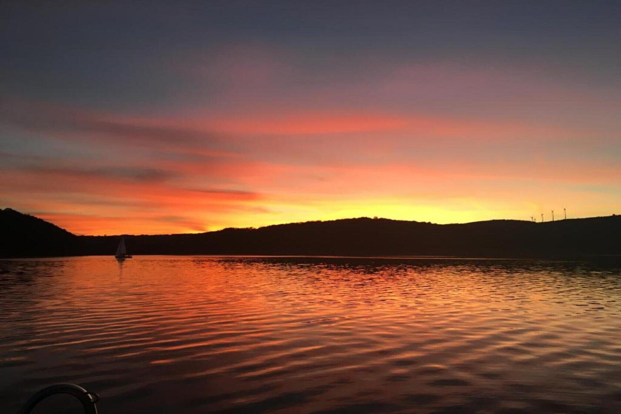 A sunset over a calm lake with a sailboat in the distance.