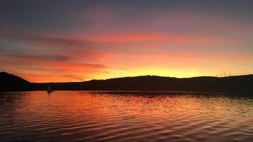 A sunset over a calm lake with a sailboat in the distance.