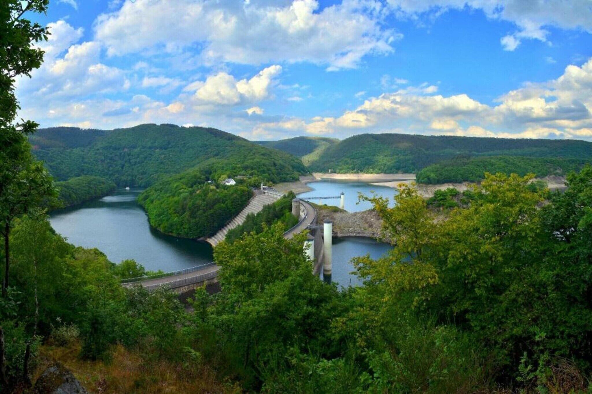 Ein Stausee mit einer Brücke und einem kleinen Gebäude, umgeben von üppigem Grün und einem Fluss.