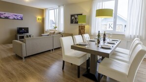 A modern hotel room with a dining area, a sofa, a TV, and a view of the outside. - Comfortable apartment in nature (Heimbach)
