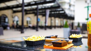 A table with food items and a bottle, set in a public space with a covered area and architectural details in the background. - Comfortable apartment in nature (Heimbach)
