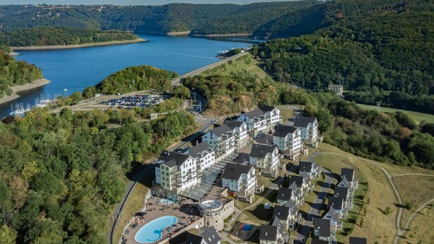 An aerial view of a residential area with a large body of water, a swimming pool, and a parking lot. - Modern penthouse with Rur valley view (Heimbach)