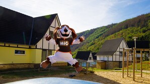 A mascot in a rural setting with a house, a playground, and a hilly landscape in the background. - Modern penthouse with Rur valley view (Heimbach)
