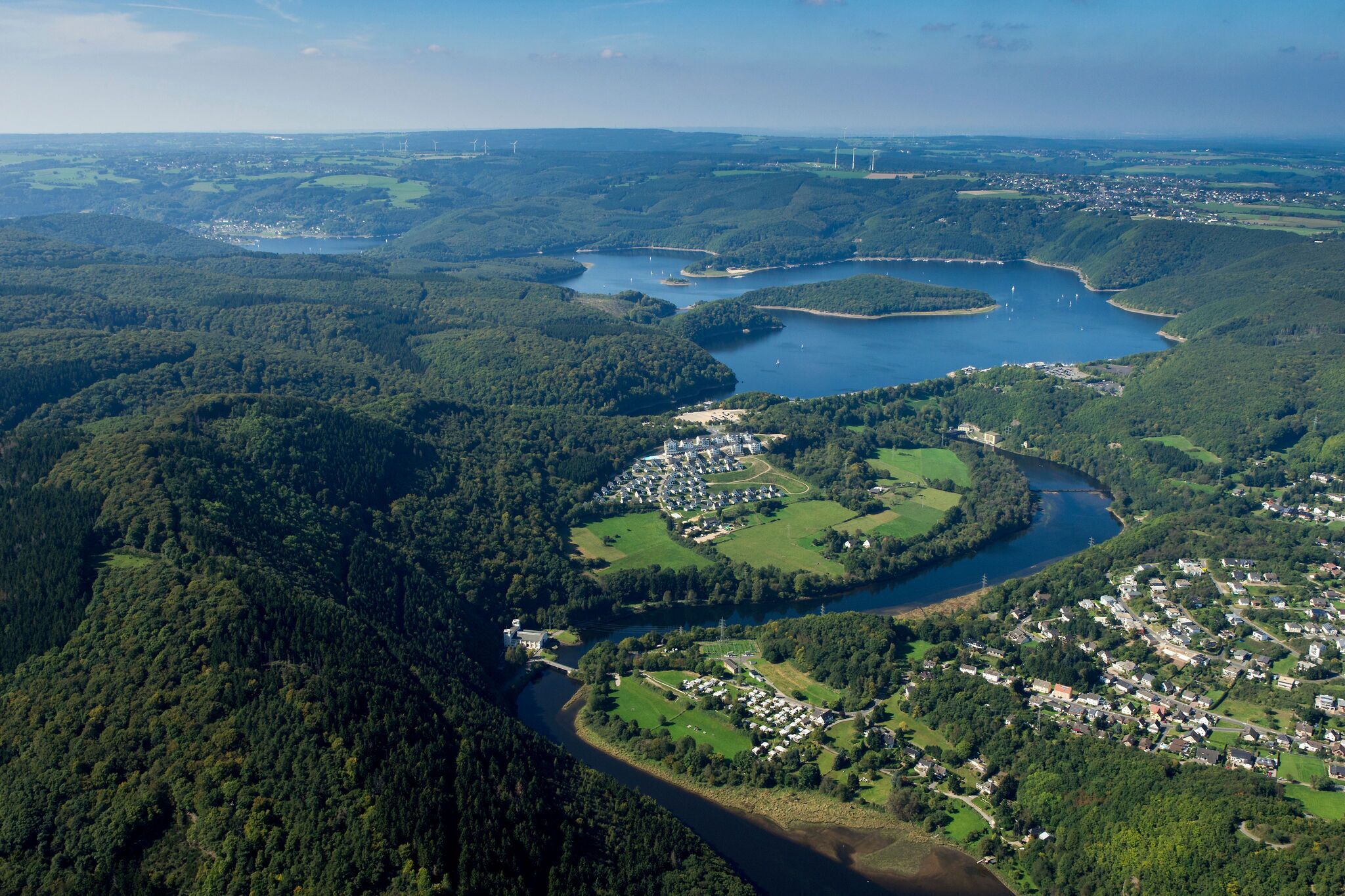 Luchtbeeld van een stad met een rivier, omringd door dichte bossen en heuvels.