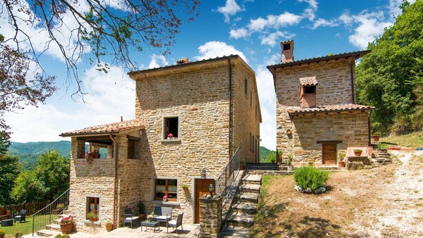 Una casa de piedra con un patio, escalones que conducen a la entrada y vistas del paisaje circundante.