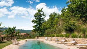 Una piscina circular de piedra con agua cristalina, rodeada de sillas de descanso y una terraza de piedra.