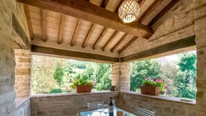 Una habitación con paredes de piedra, una mesa de vidrio y sillas, una botella y dos plantas en macetas.