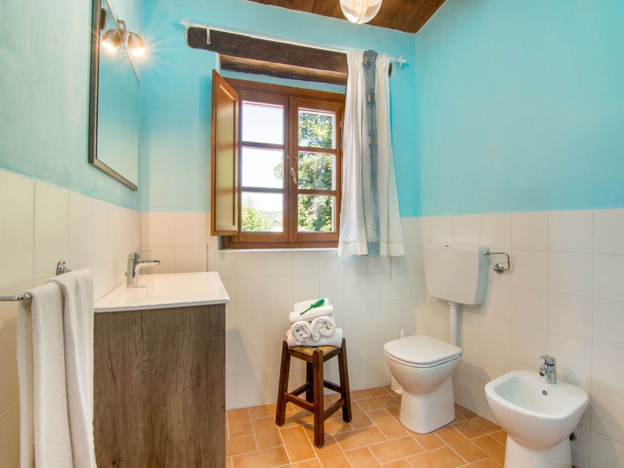 Une salle de bain avec un meuble-lavabo en bois, des toilettes, un bidet et une fenêtre avec des rideaux.