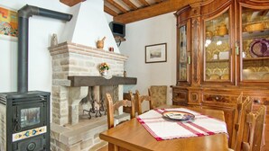 Un interior rústico con chimenea de piedra, mesa de comedor de madera y un aparador con puertas de cristal.