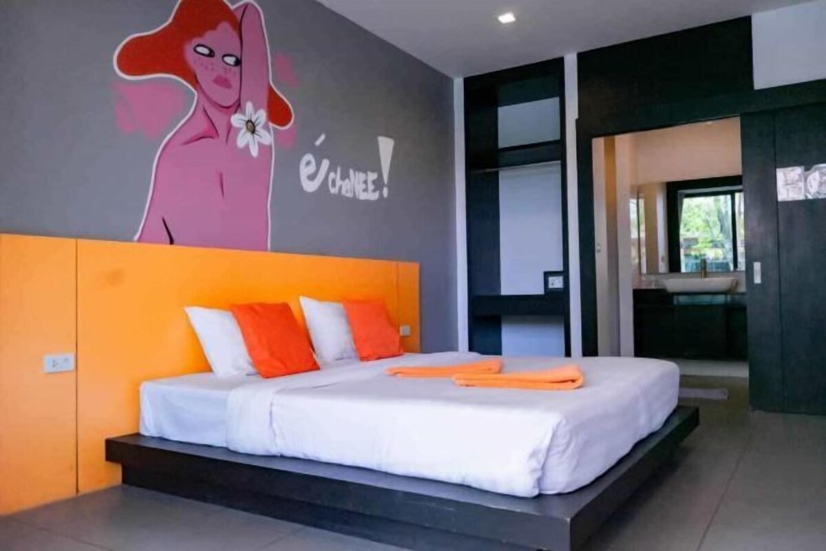 A modern bedroom with a large bed, orange headboard, and a wall mural.