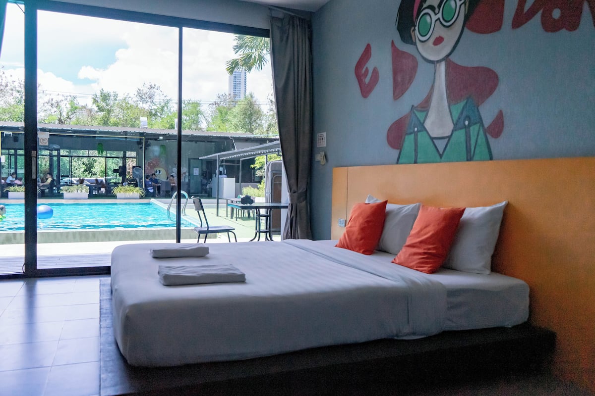 Une chambre d’hôtel avec un grand lit, une vue sur la piscine et une fresque murale.
