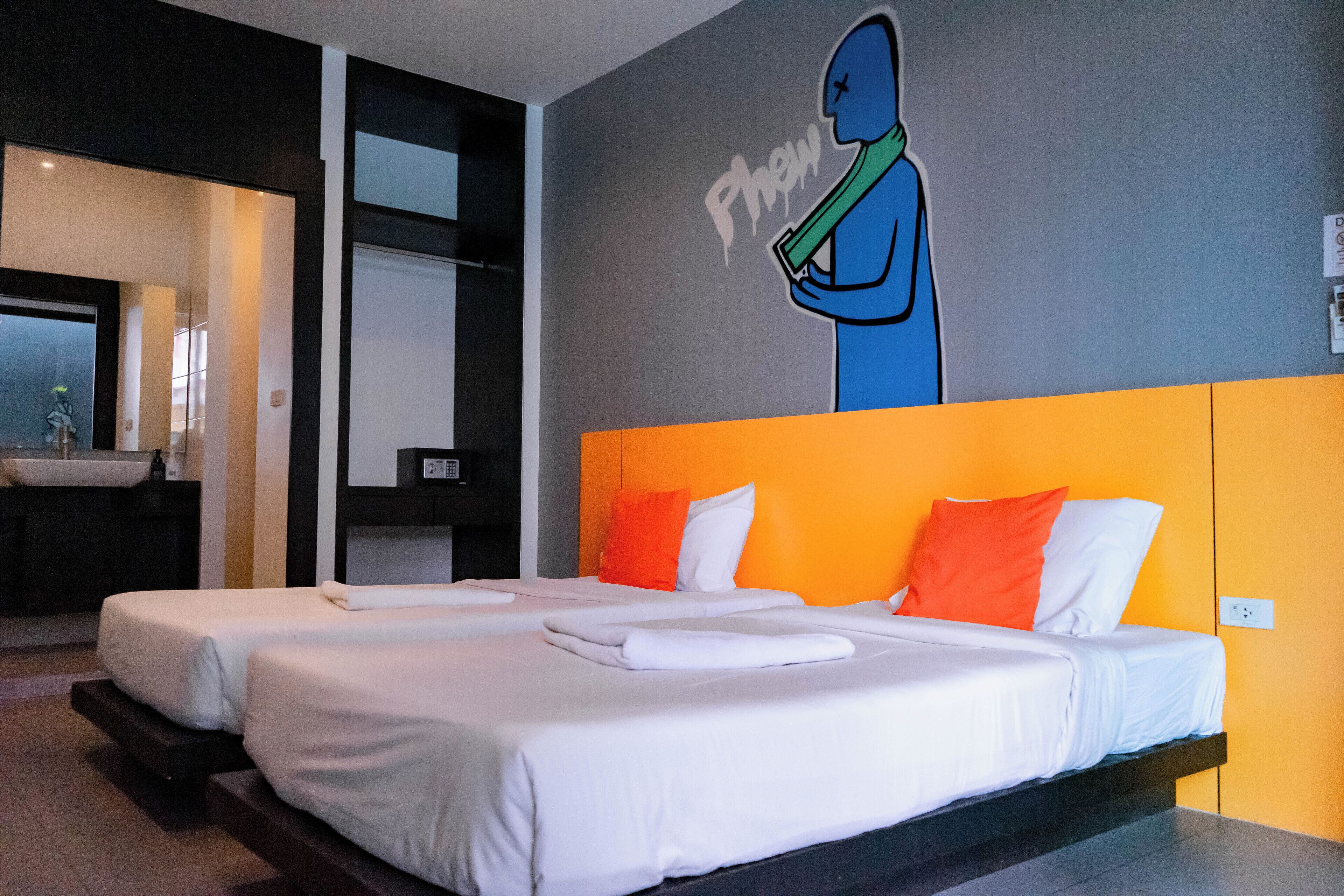 A hotel room with two beds, an orange accent wall, and a mural of a person holding a green object.