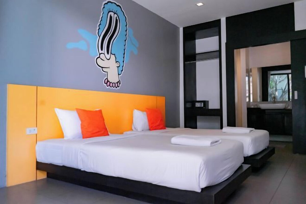 A modern hotel room with two beds, a large mural, and a bathroom visible through an open door.
