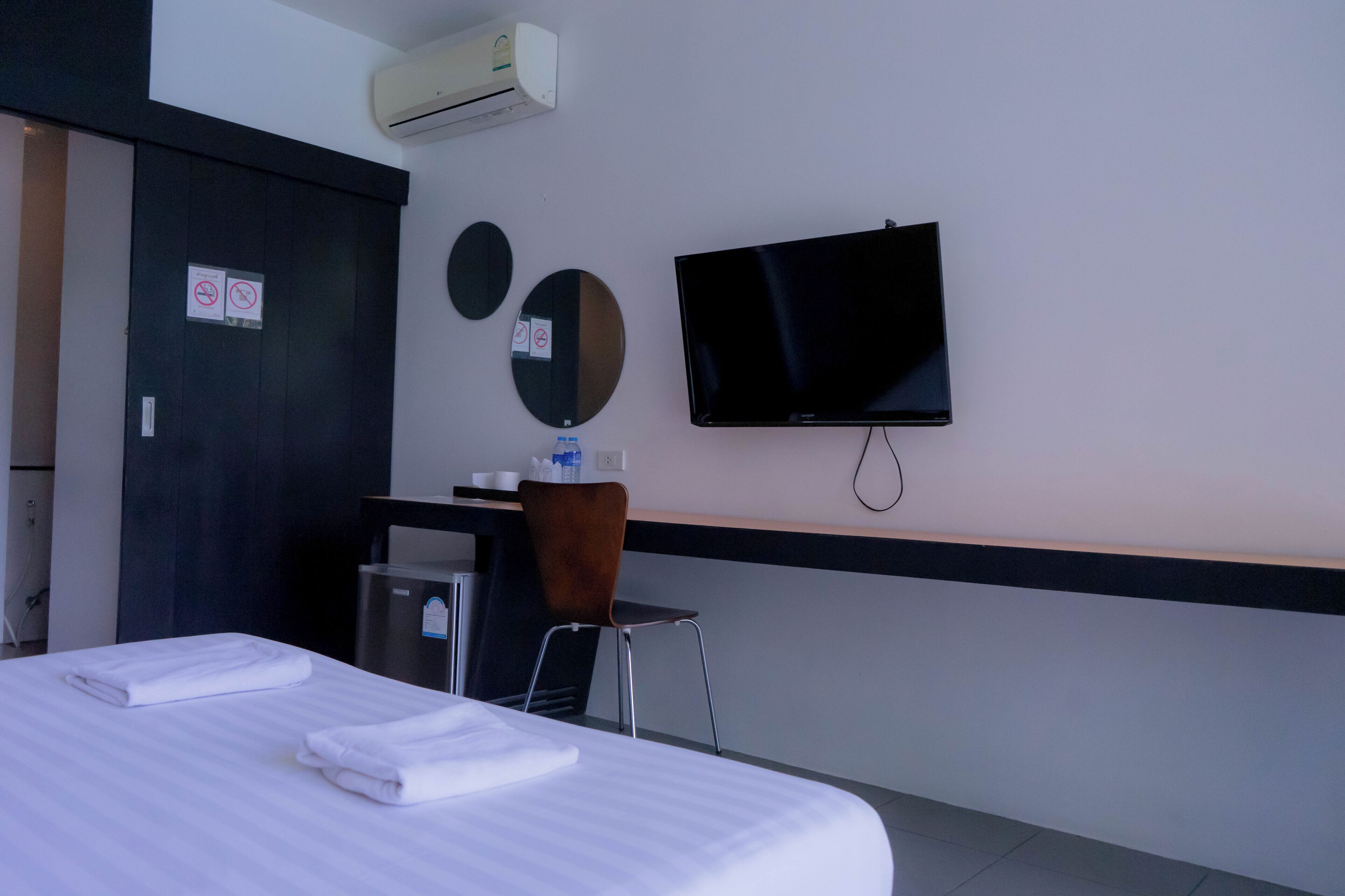 A hotel room with a bed, a desk, a chair, a TV, and an air conditioning unit.