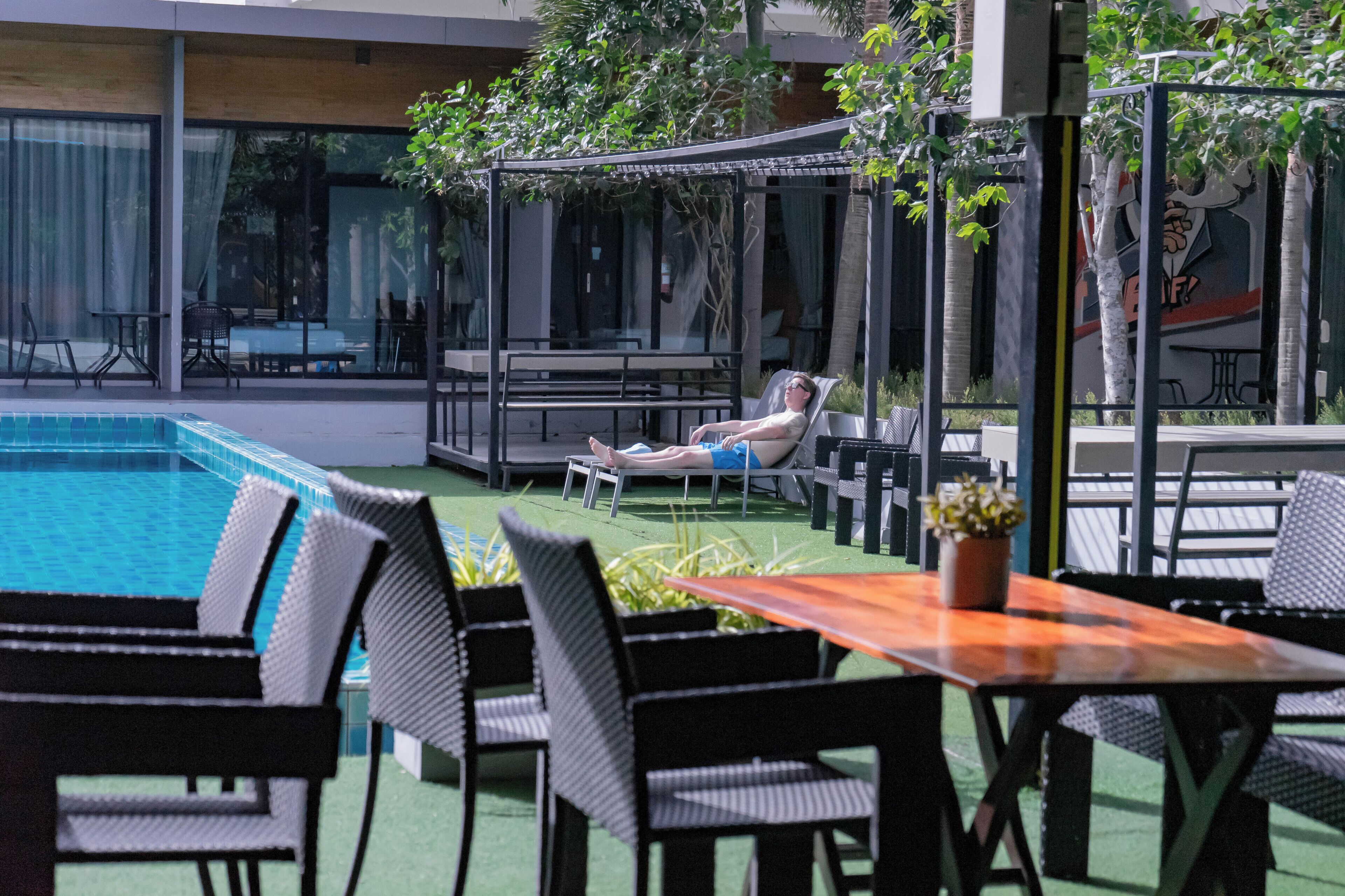 Uma área à beira da piscina com espreguiçadeiras, uma mesa e um espaço coberto para sentar.