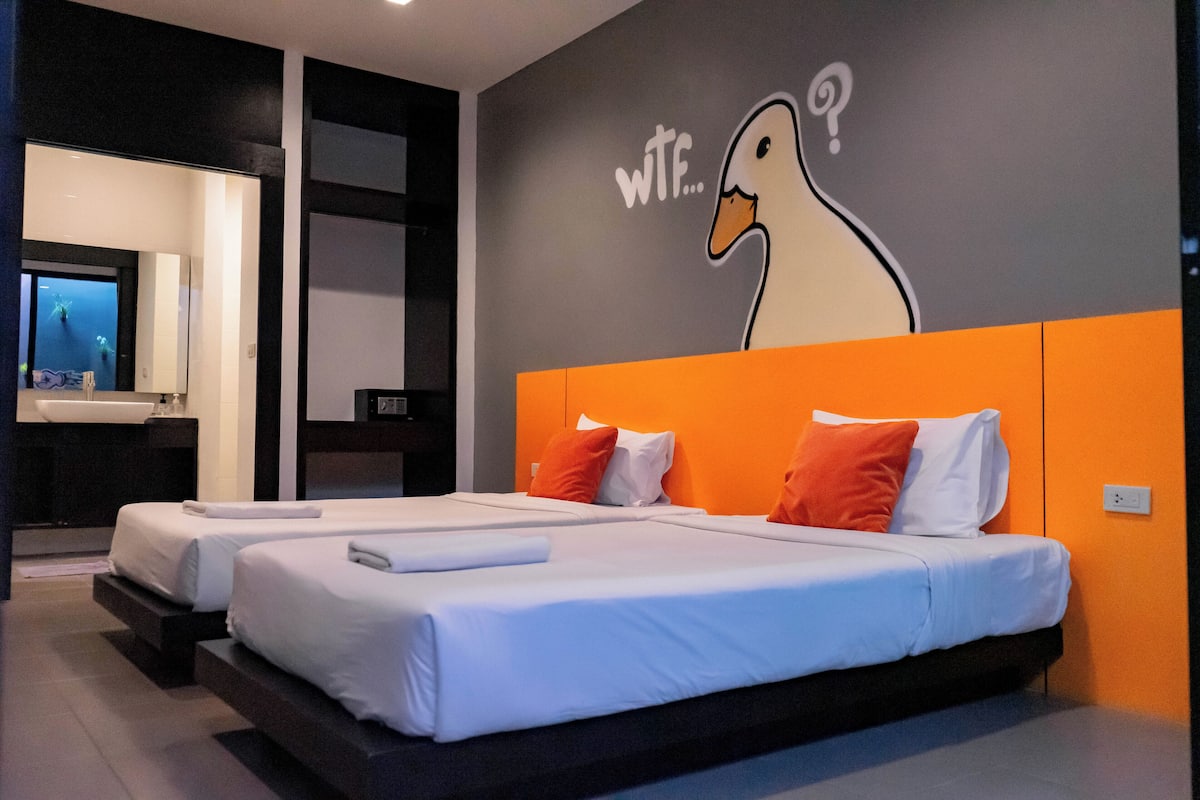 Une chambre d’hôtel avec deux lits, un grand miroir et une fresque murale représentant un canard, sur laquelle on peut lire le texte : « WTF...? ».