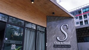 A Club & Hotel sign with a large 'S' logo, a wooden ceiling, and a modern building facade in the background.