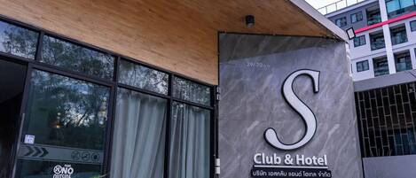 A Club & Hotel sign with a large 'S' logo, a wooden ceiling, and a modern building facade.