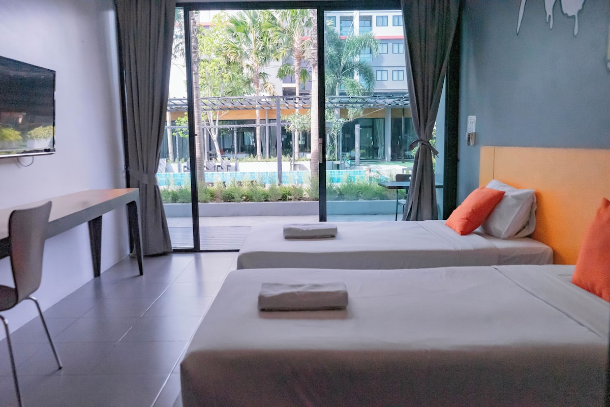 Une chambre d’hôtel avec deux lits, un bureau et une vue sur une piscine et les bâtiments environnants.