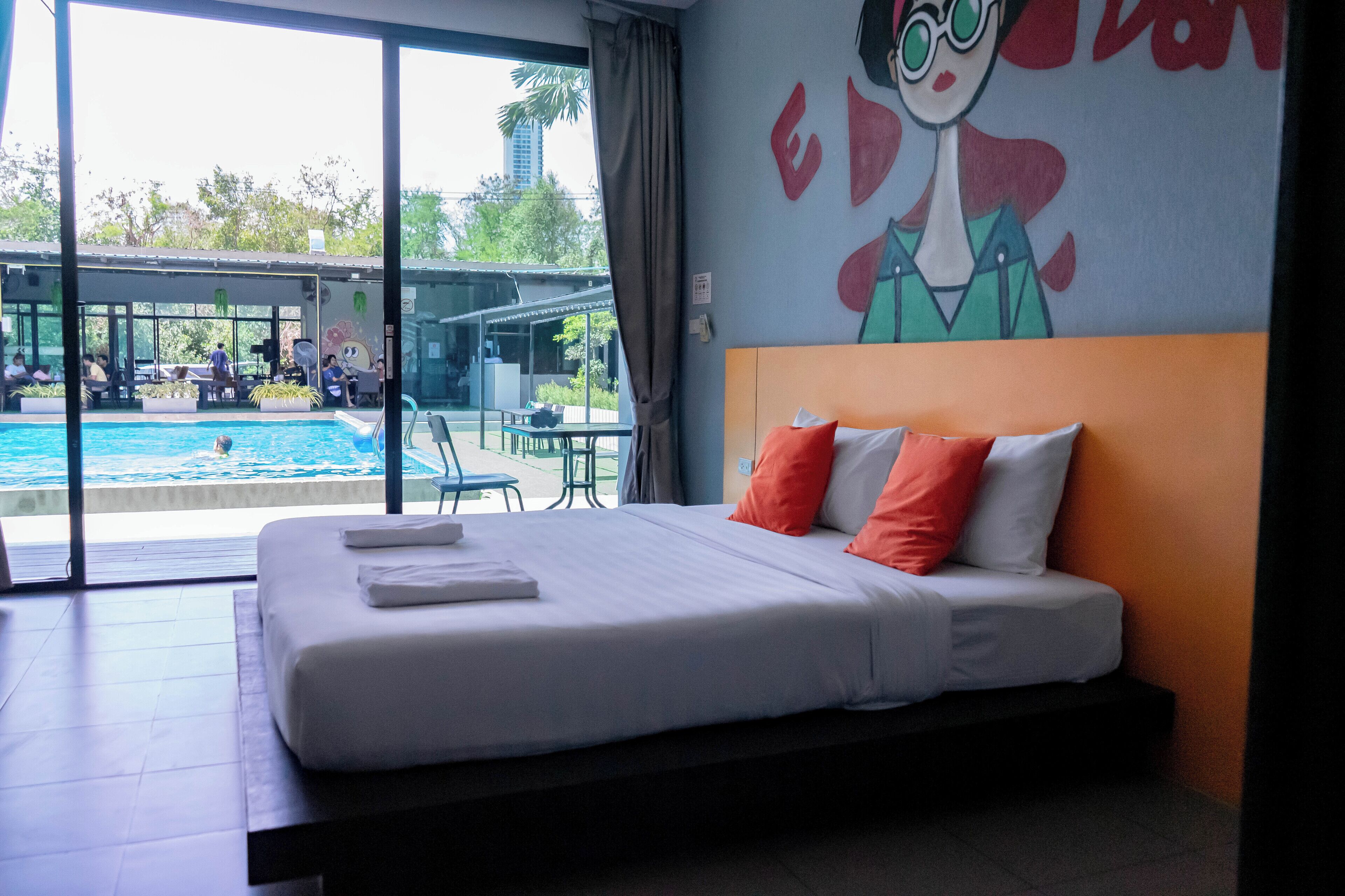 A hotel room with a bed, a view of a swimming pool, and a mural on the wall.