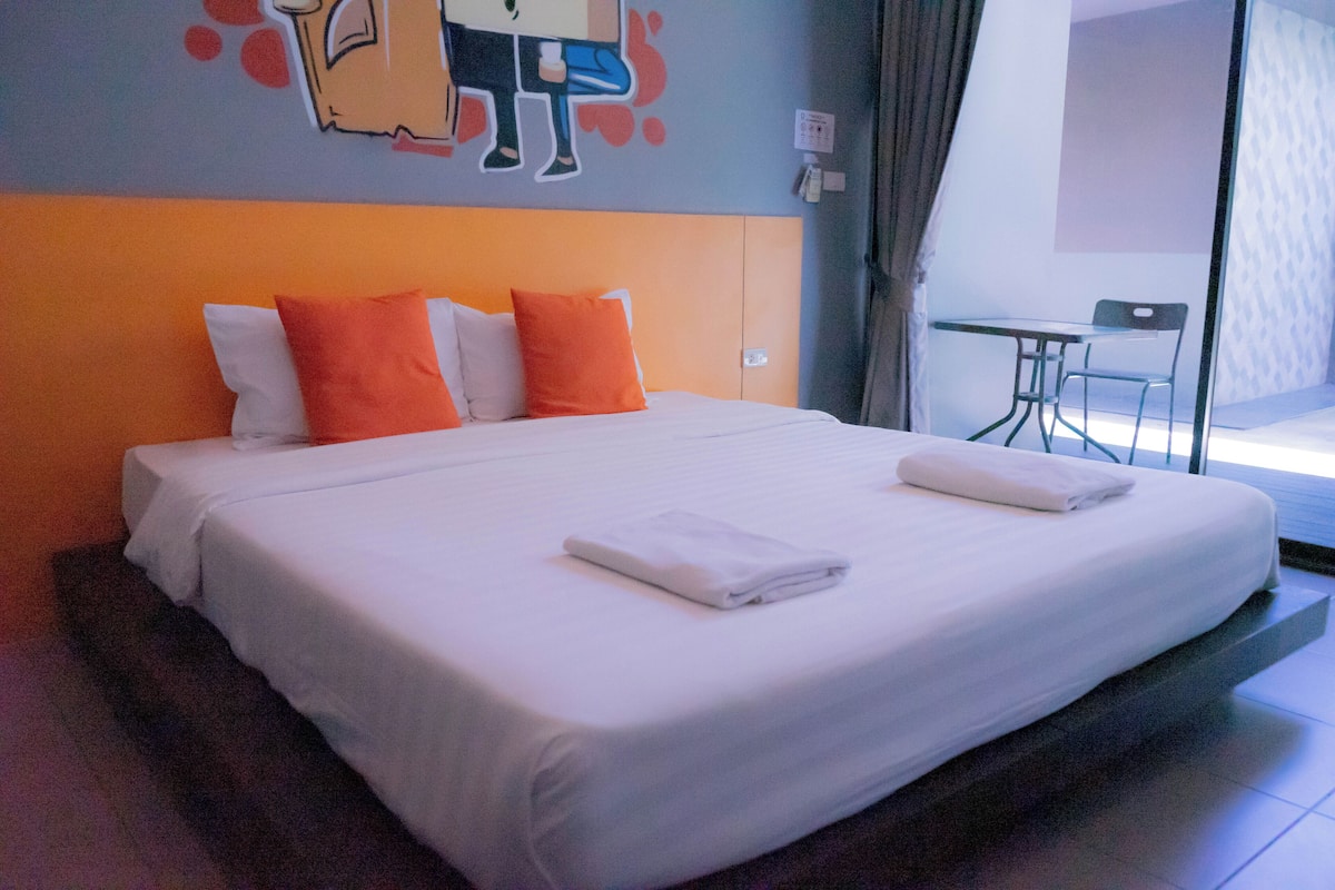 Une chambre d’hôtel avec un grand lit, des oreillers orange et blancs, une petite table et une chaise.