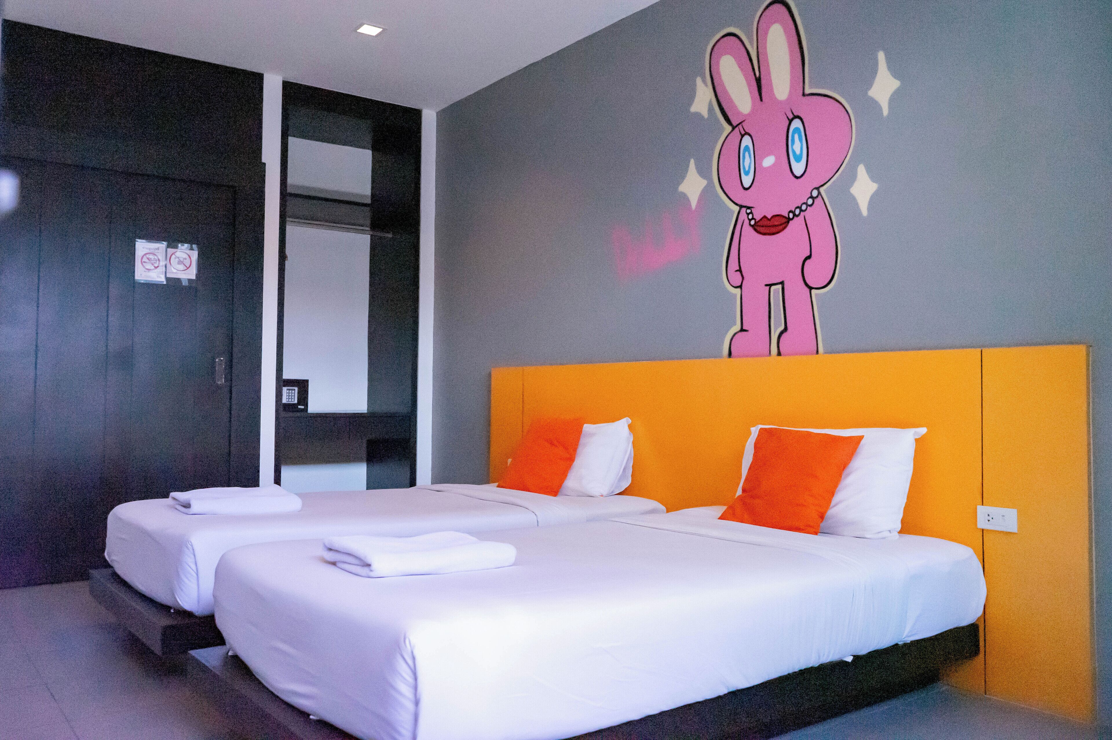Une chambre d’hôtel avec deux lits, une grande fresque murale représentant un lapin de dessin animé et un décor moderne.