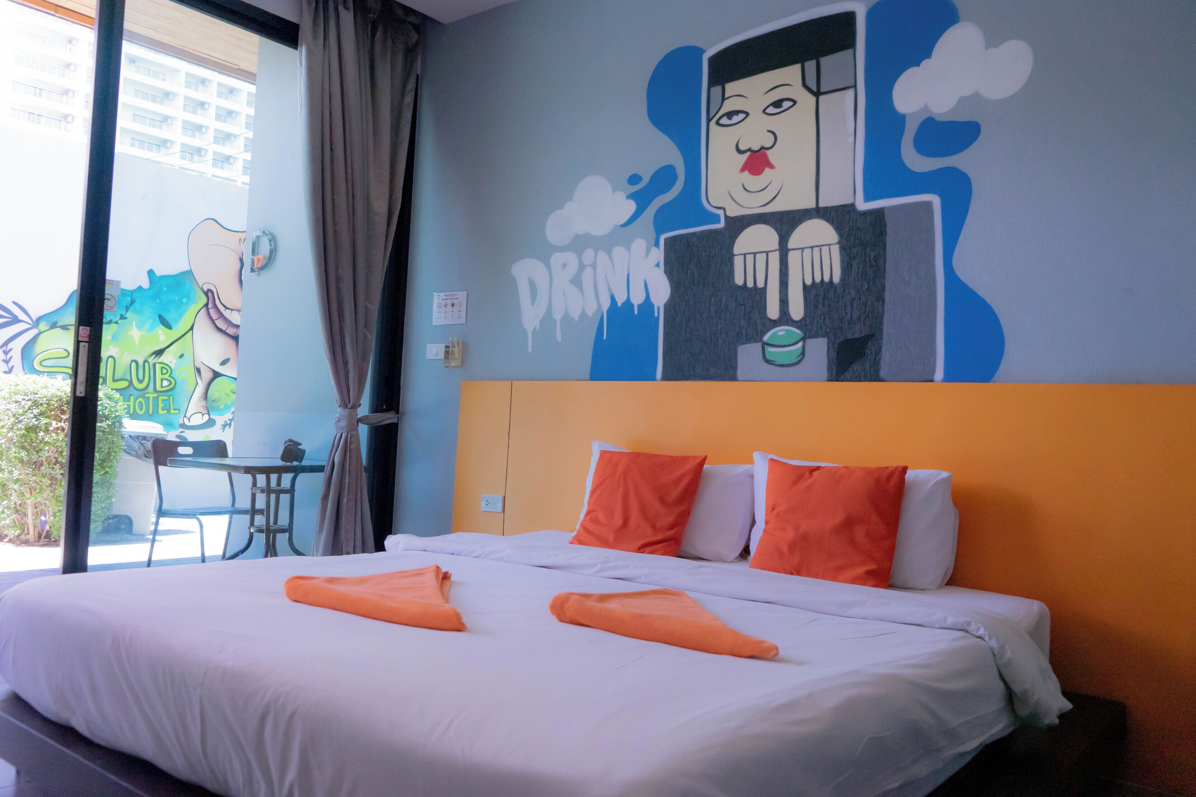 A hotel room with a bed, orange pillows, and a mural on the wall.
