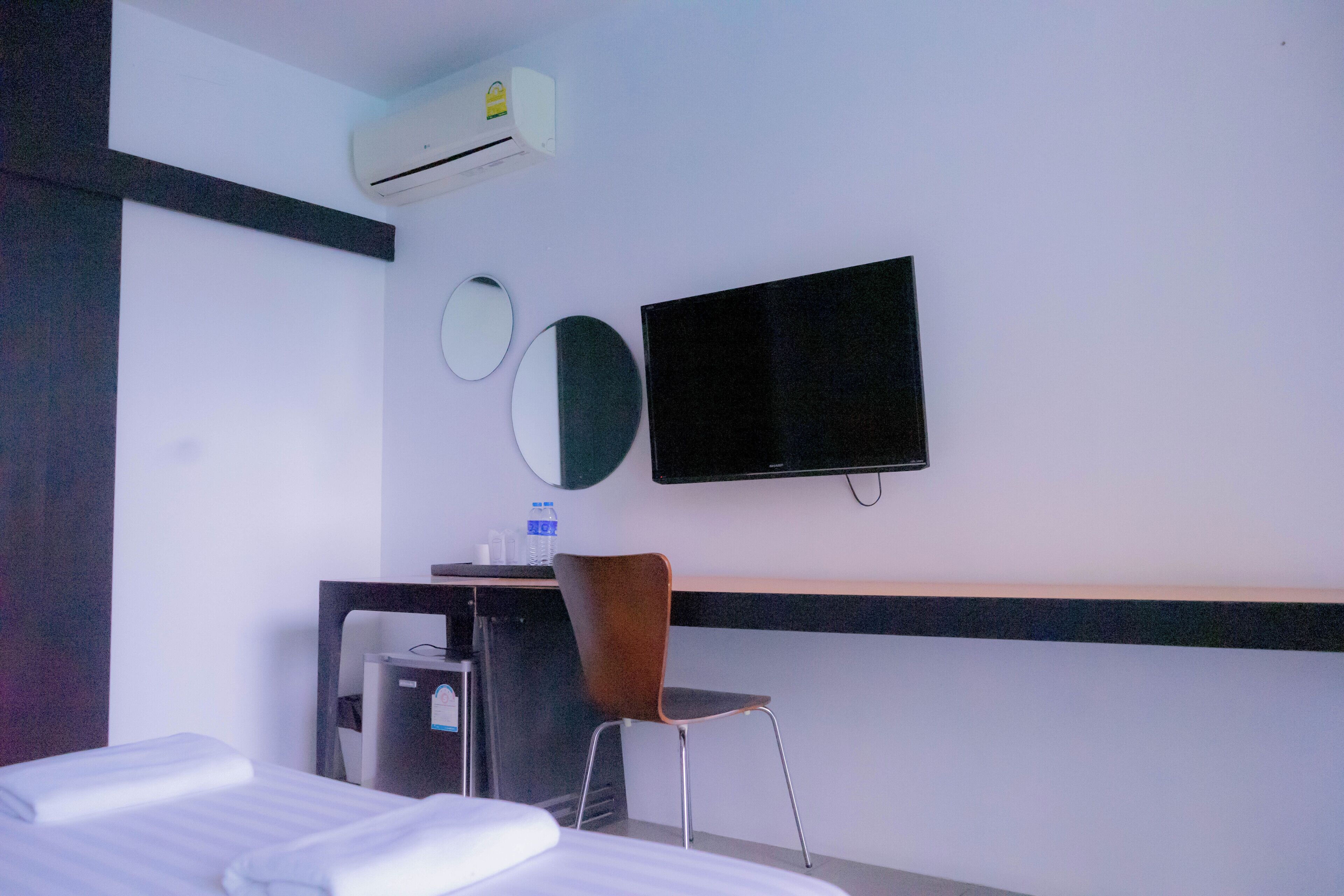A hotel room with a bed, a desk with a chair, a flat-screen TV, an air conditioner, and two wall-mounted mirrors.