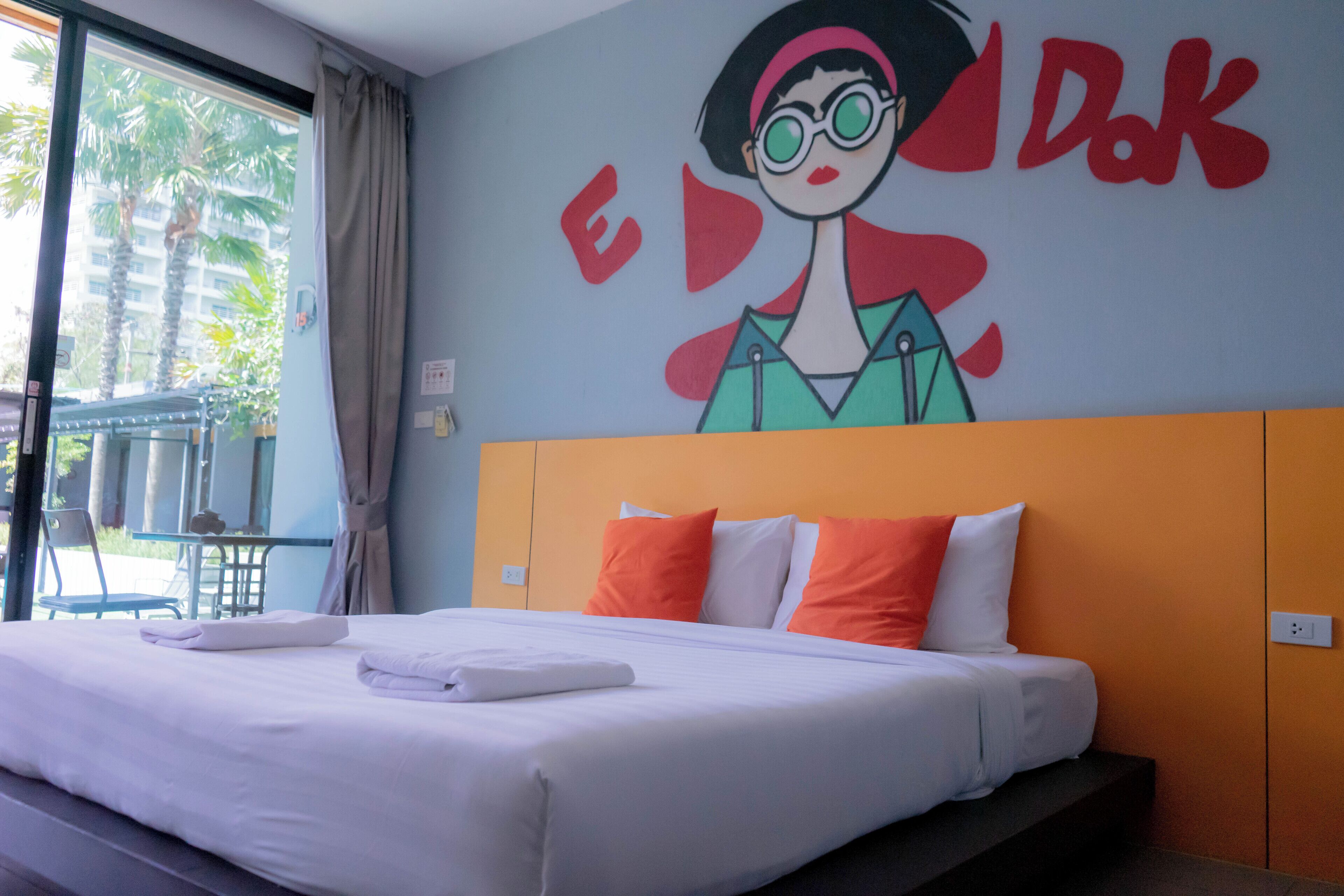 Hotelkamer met een bed, oranje hoofdeinde en een muurschildering van een stripfiguur.