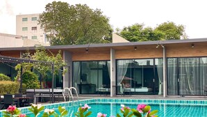 A modern hotel with a swimming pool, outdoor seating, and large windows.