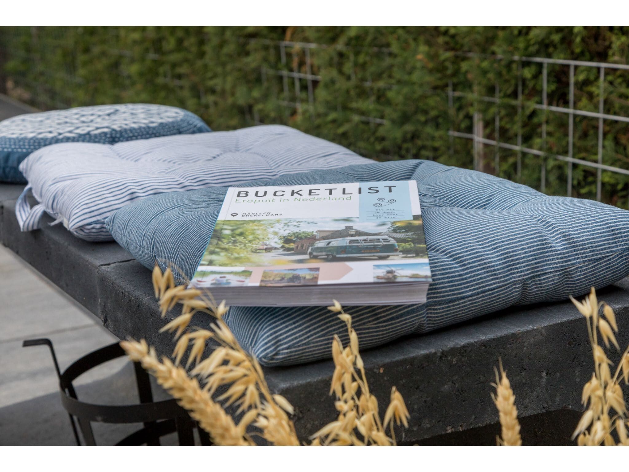 A brochure titled "Bucketlist Eropuit in Nederland" on a bench with blue and white striped cushions.