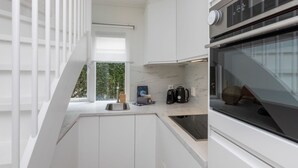 A modern kitchen with white cabinetry, a built-in oven, and a window overlooking greenery.