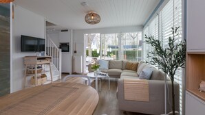 A modern living room with a wooden dining table, a sofa, and a TV mounted on the wall.