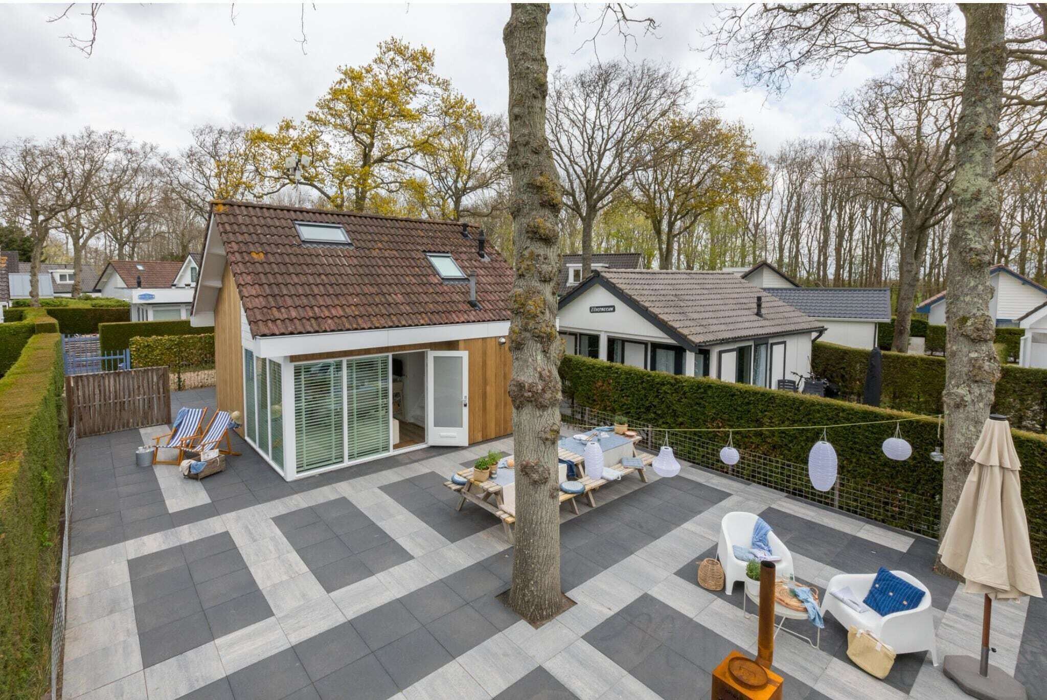 Ein modernes Haus mit einer gefliesten Terrasse, einem Essbereich und Sitzmöglichkeiten im Freien.