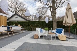 An outdoor patio area with a dining table, two white chairs, a small round table, and a potted plant.